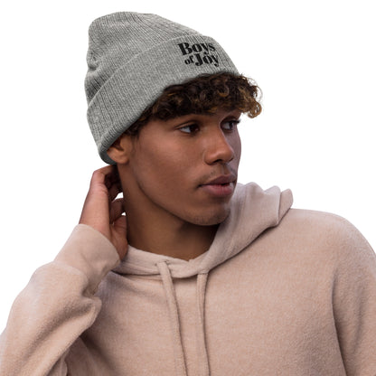 Model in beige hoodie wearing light-grey melange ribbed beanie with ‘Boys of Joy’ logo, three-quarter profile.